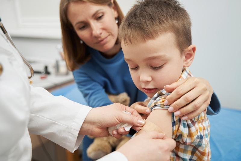 a boy getting a bandaid put on while his mom watches